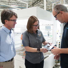 Three people on a manufacturing floor discussing a new product