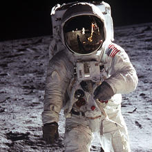 Photo of man in white space suite on surface of moon at night.