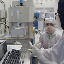 Man and woman in lab gear in front of computer screen in clean room