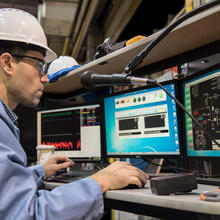 NIST Researcher in a hard hat watches three monitors that show data from a fire burn.