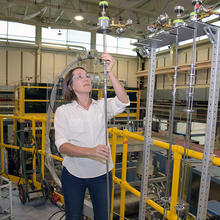 kate Ross holds a long pole used to put samples in front of a beam of neutrons  in the main hall at the NIST Center for Neutron Research. 