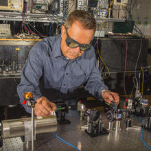 Man in striped shirt wearing laser safety glasses working with laser table in laboratory.