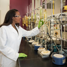 A chemist stands in a white coat before a bunch of beakers.