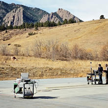 Mountains in the background. Left: rolling cart with equipment. Tall tripod. Right: Two men with another rolling cart of equipment.