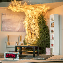 A Christmas tree is engulfed in flames. To the left is a chair. In front is a coffee table, rug and fishbowl. To the right is a tall bookshelf. There are 3 wrapped presents under the tree. A timer reads 8:04 seconds.