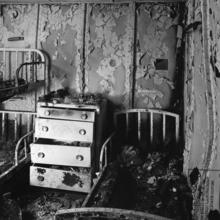 Black and white photo of post fire aluminum bedroom replica of SS united States ship in 1950. To the right and left there are burned bed frames and in the middle a burned dresser.