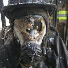 Closeup of firefighter face mask covered in char from fire burn. The rest of the uniform is also black, but in tact. 