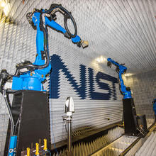 Room covered with spiky white insulation with large blue robotic arms located on the left and the right. Small horn antenna is attached to tip of left robotic arm.