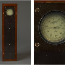 A long, thin, rectangular wooden box framing a metal plate with an circular analog gauge reading from 1 to 100. Printed on the gauge are the name "B.C. Ames Co., Waltham, Mass. U.S.A," and "1"/1000," and a handwritten "28586 B."