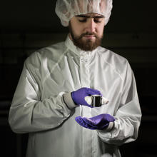 Man in clean suit and purple gloves holding a kilogram sample with tongs