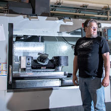 Luther Vulgamott stands in front of a five-axis computer numerical control machine