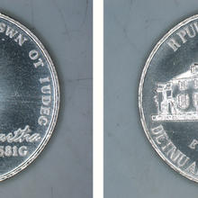 The nickel prototype, which is the same shape and size as a regular nickel, but instead of Thomas Jefferson has a profile of Martha Washington in a mob cap and dummy text instead of "E Pluribus Unum."