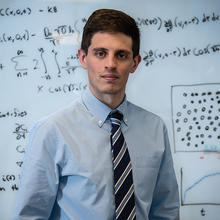 Mathematician Ryan Evans in front of a whiteboard covered in mathematical equations