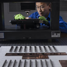 A man with green gloves looks at an item under a microscope