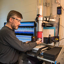 Scientist puts material down below a tube. Background: computer screen