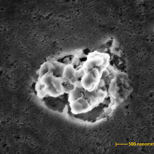 An electron micrograph showing a globular cluster of silver nanoparticles atop the surface of a cutting board from which it was scratched off.