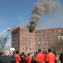 High rise building with smoke coming out of upper windows. Two people in bucket trucks.