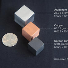 three metal cubes: aluminum, copper and carbon. Next to the cubes is a quarter to show relative size and mass. All three are one mole's worth of atoms.