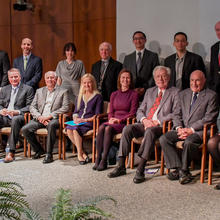 6 men and 3 womens seating with 8 men and 1 woman standing behind them