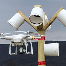 A drone in flight approaches a bucket-shaped target attached to a pole during an evaluation on the NIST performance test course.
