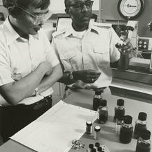 Two men in a lab with vials of oil in front of them.