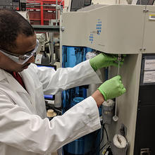 man in a white lab coat and safety goggles loads a metal oxide framework material into a testing machine