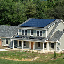 Photograph of large residential-style home with blue tile roof and solar panel in suburban campus setting.