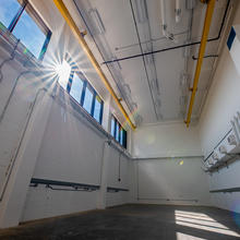 A large empty room has white walls and windows near the ceiling with sun shining in.