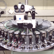 Massively parallel wafer-level long-term reliability test system featuring 30 fully functioning mini probe stations each supporting 100 probe pins with all the supporting stress/measure electronics integrated (without cables). 