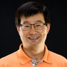 headshot of man in orange shirt. black background.