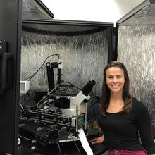 A woman (Callie Higgins) stands in front of a piece of photopolymerization equipment. 