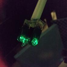 Tiny glass vial in holding device glows green in dark photo.