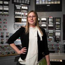 A woman stands in front of a wall full of knobs and switches.