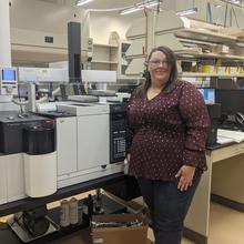 Cheryle Beuning poses in front of scientific equipment, wearing safety goggles.