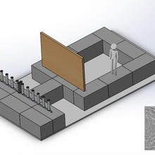 Human figure stands facing large wooden board. Behind that is a row of tubes sticking up from a base.