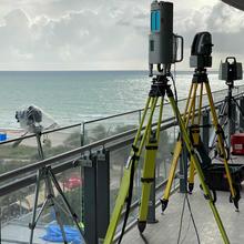 Equipment stands on tripods on a balcony with the beach and sea in the background.