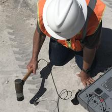 Person in hard hat is tapping concrete with a hammerlike device.