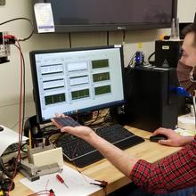 NIST researcher Andrew Shore holds a miniature high efficiency solar device as it charges a sensor using indoor light as an energy source.