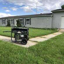 A portable generator is placed on the sidewalk far away from a home. 