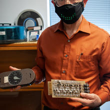 Paul Black poses holding vintage computing devices.