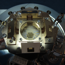Ion trap is tiny chip held in place as part of a larger metal scientific device.