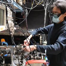 A person wearing safety goggles works at a table of scientific equipment.