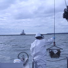 A researcher stands on a boat reaching for a cable holding a grabber device. 