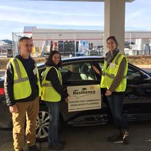 Three people in high-vis vests stand near a car that has a sign on the door: Center for Community Resilience Planning.