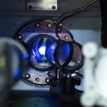 Blue light shines out of a circular opening in an atomic clock. 