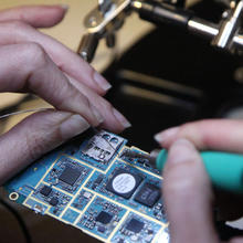 A closeup photograph of person's hands as they solder a wire onto a circuit board.