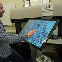 Greg Fiumara, in an office setting, looks at a large screen showing a close-up fingerprint.