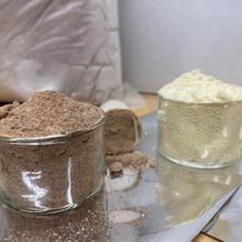 Two open glass containers hold powder, one brown and one white, with half-filled plastic scoops next to each. 