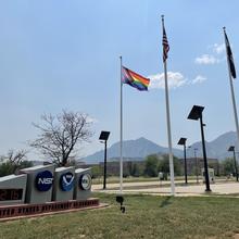 Entrance signs for NIST and NOAA are in the left foreground, with flagpoles, mountains and blue sky in the background.