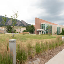 Sidewalk in foreground, with an angular office building to the right and mountains and a cloudy sky in the background.